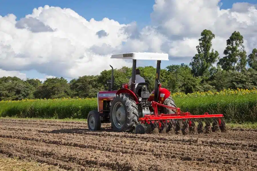 A red tractor clearing and preparing agricultural land for farming in a rural area, illustrating mechanized large-scale agriculture